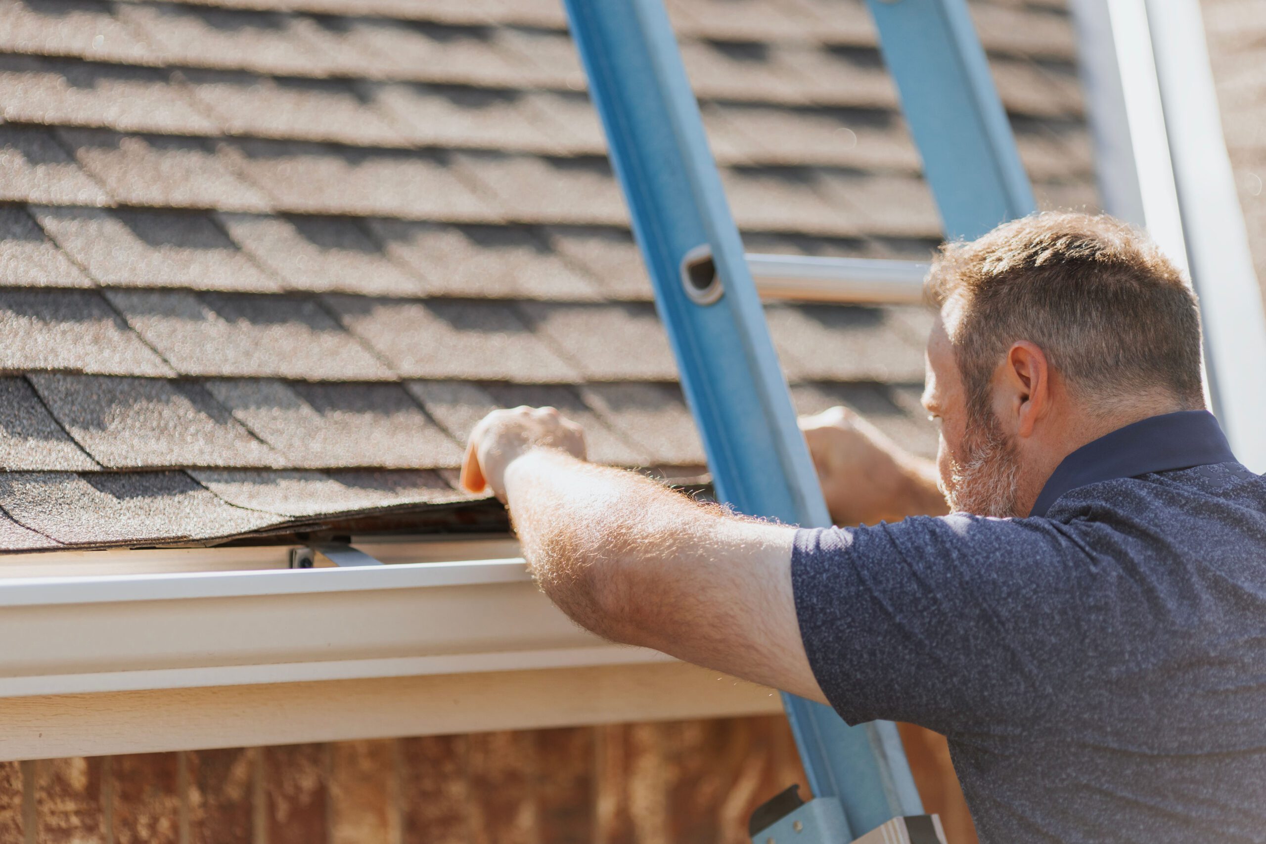 A roofing professional inspecting damaged shingles on a residential roof in Oklahoma City after a storm.