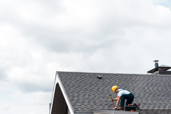 repairman in helmet holding hammer while repairing roof