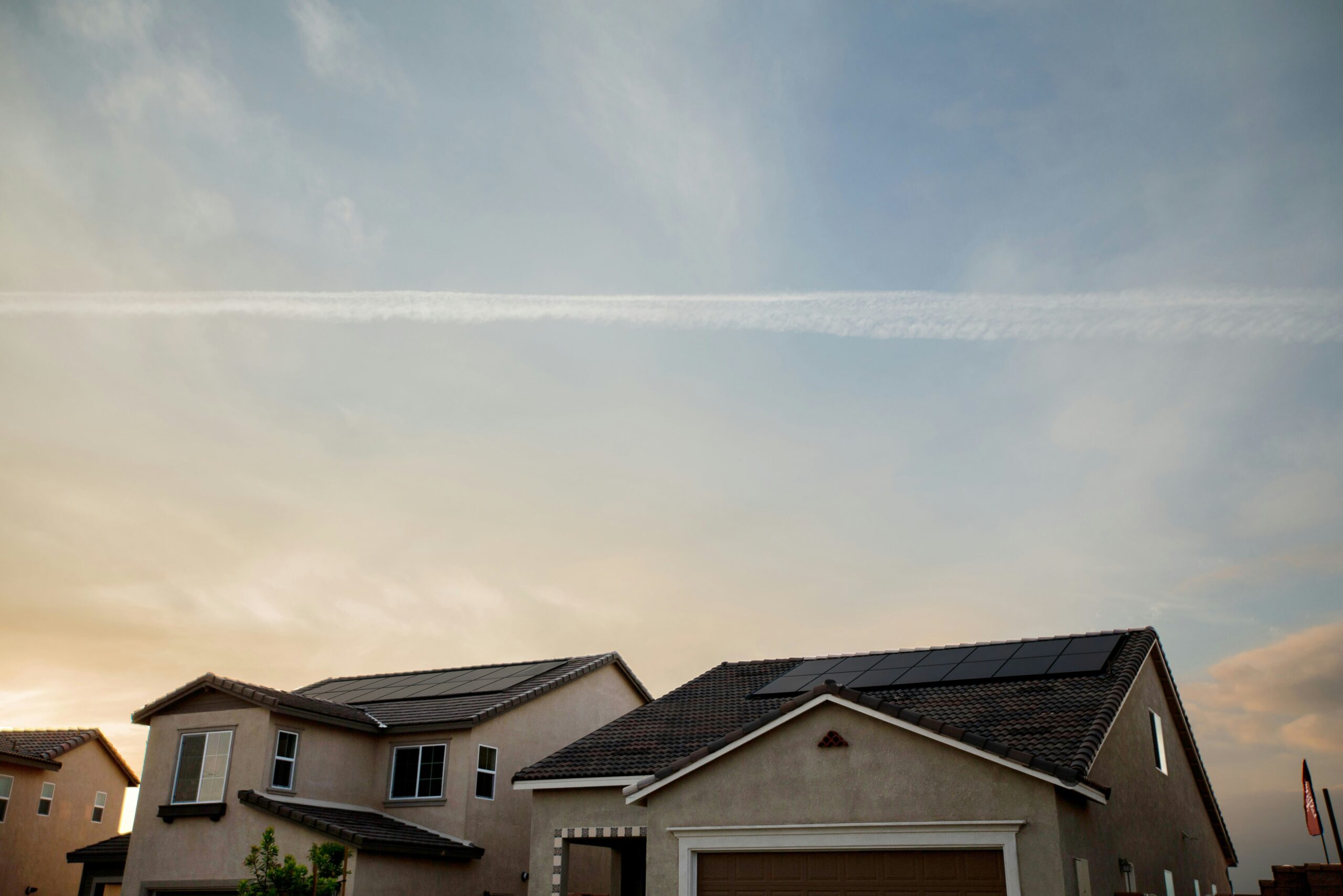 Two suburban homes with tile roofs at sunset, one featuring solar panels under a partly cloudy sky.